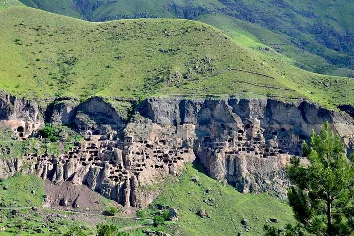 Wide landscape view of the Vardzia cave city carved into the green hillside